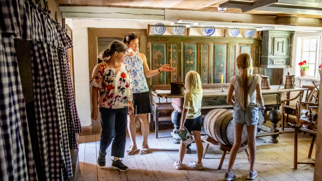 To kvinder og to piger betragter interiøret i et af de gamle huse på frilansmuseet.