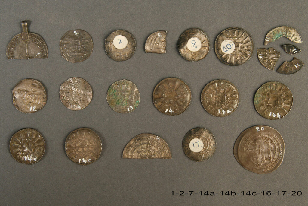 Sølvmønter fra Vålseskatten. Nogle af mønterne er klippet itu som betalingssølv. Det var sølvet, som havde værdi, ikke mønten i sig selv. En af mønterne har fået en øsken påsat, så den kunne bruges som halssmykke. Foto: Nationalmuseet.