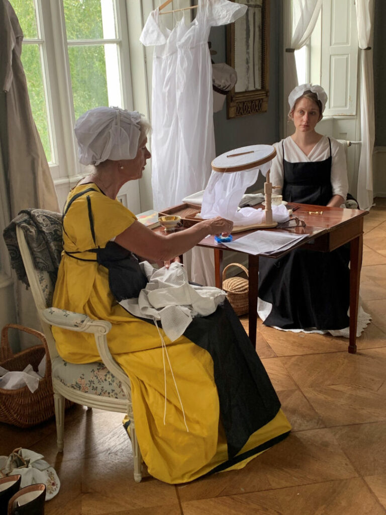 Two women in period costumes at Pederstrup. Both busy with sewing.