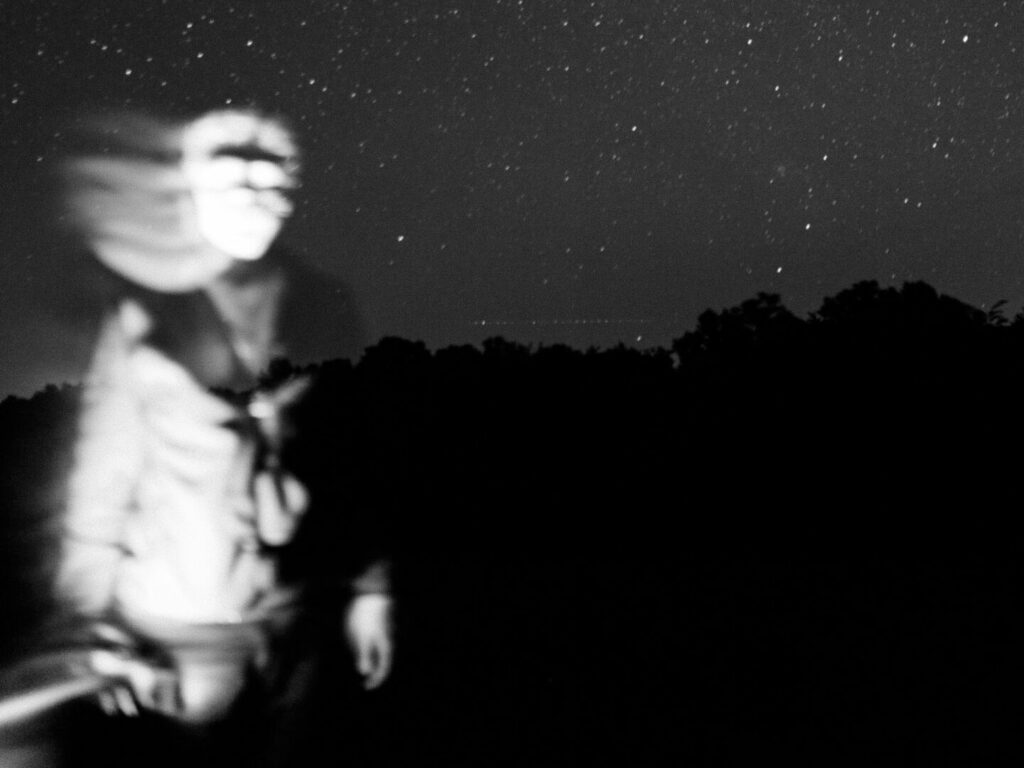 Verschwommener Umriss einer humanoiden Figur auf dem Hintergrund eines dunklen Himmels.