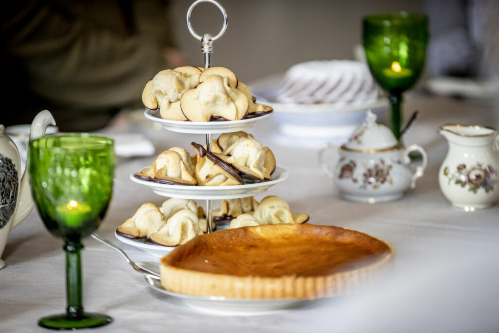 Udsnit af kagebord med opsats med napoleonshatte samt blomstret porcelæn med guldkant.
