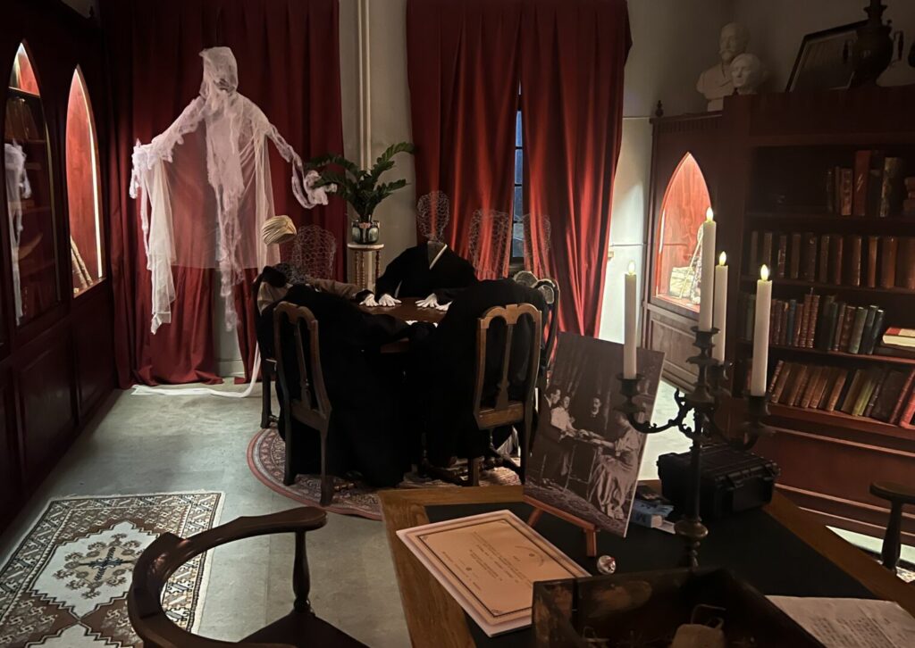 Interiør fra en af Cornelius' stuer i Museum Obscurum. Man aner en spøgelseslignende gestalt i baggrunden.